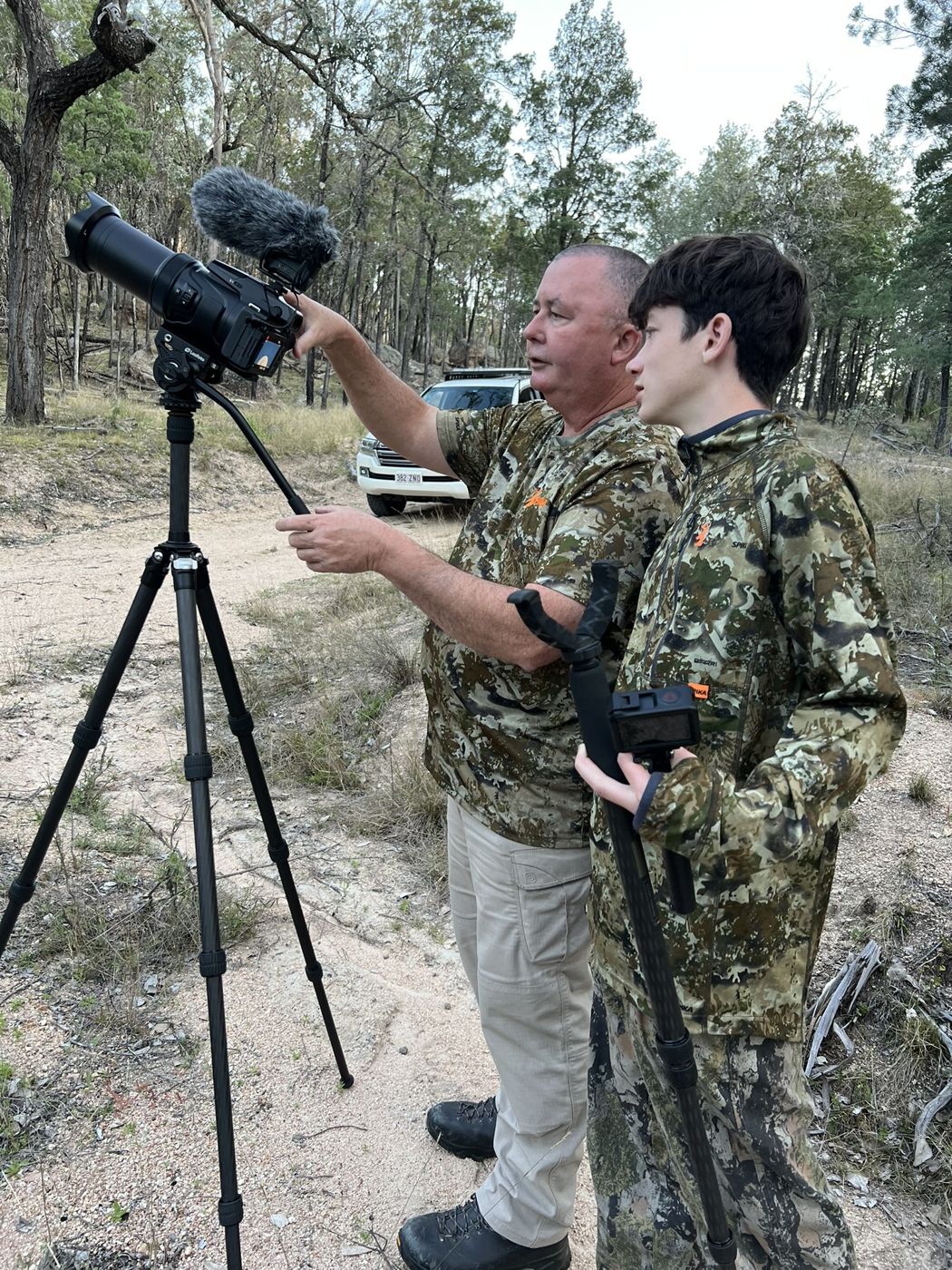 Glenn showing Ethan a camera set up on a tripod on a bush track