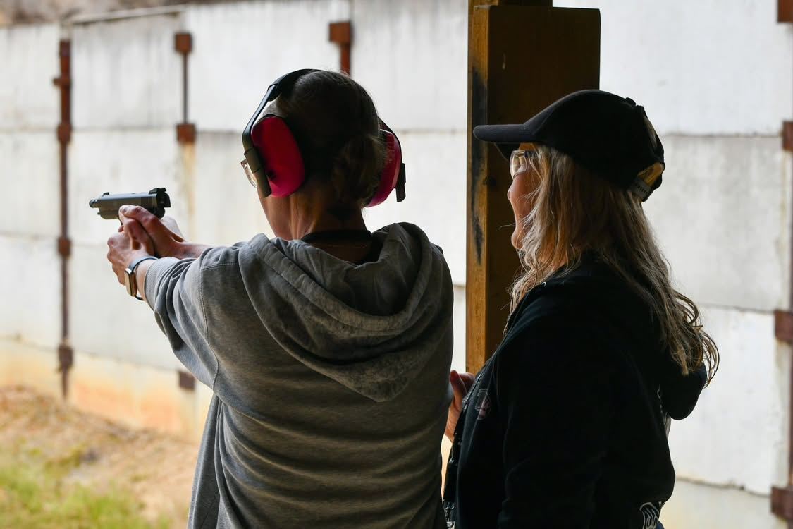 An instructor watching a woman in a grey hoodie fire a pistol