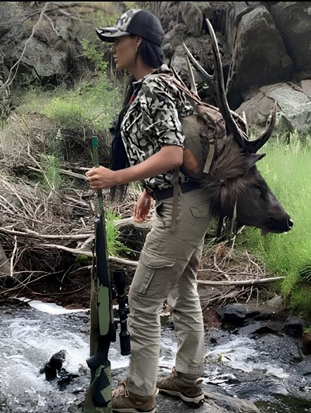 Sharelle Galea carrying a sambar deer out across a creek with her rifle in hand