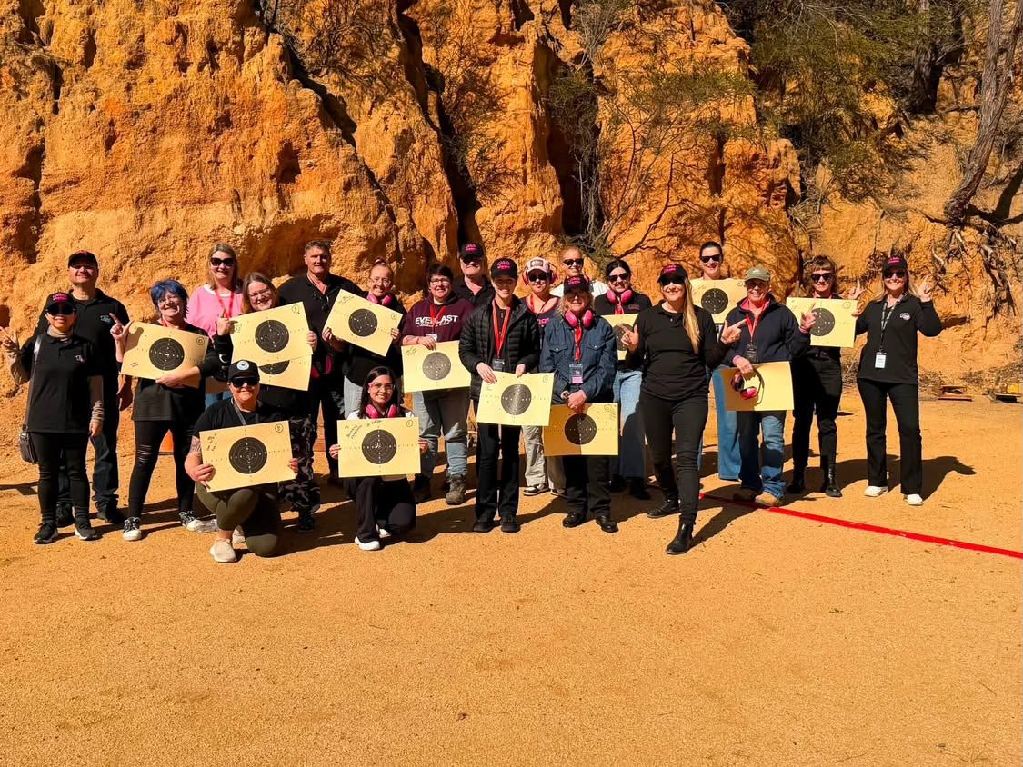 A large group of women holding up their targets in front of an orange sandstone cliff