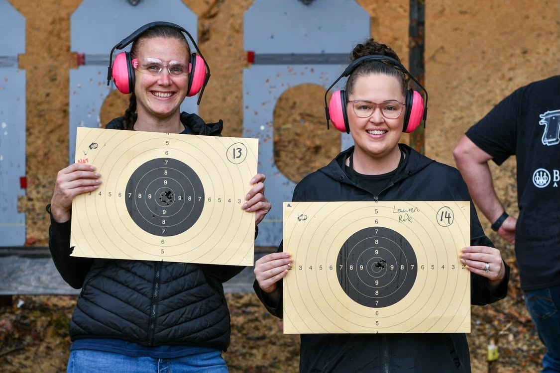 Two smiling women in pink earmuffs holding up their targets