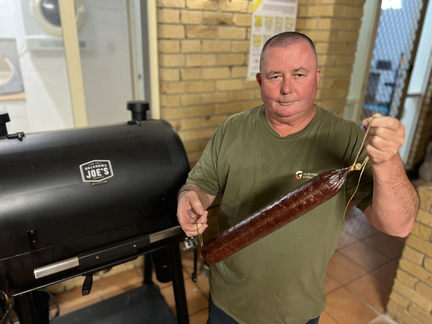 Glenn holding a salami beside a smoker