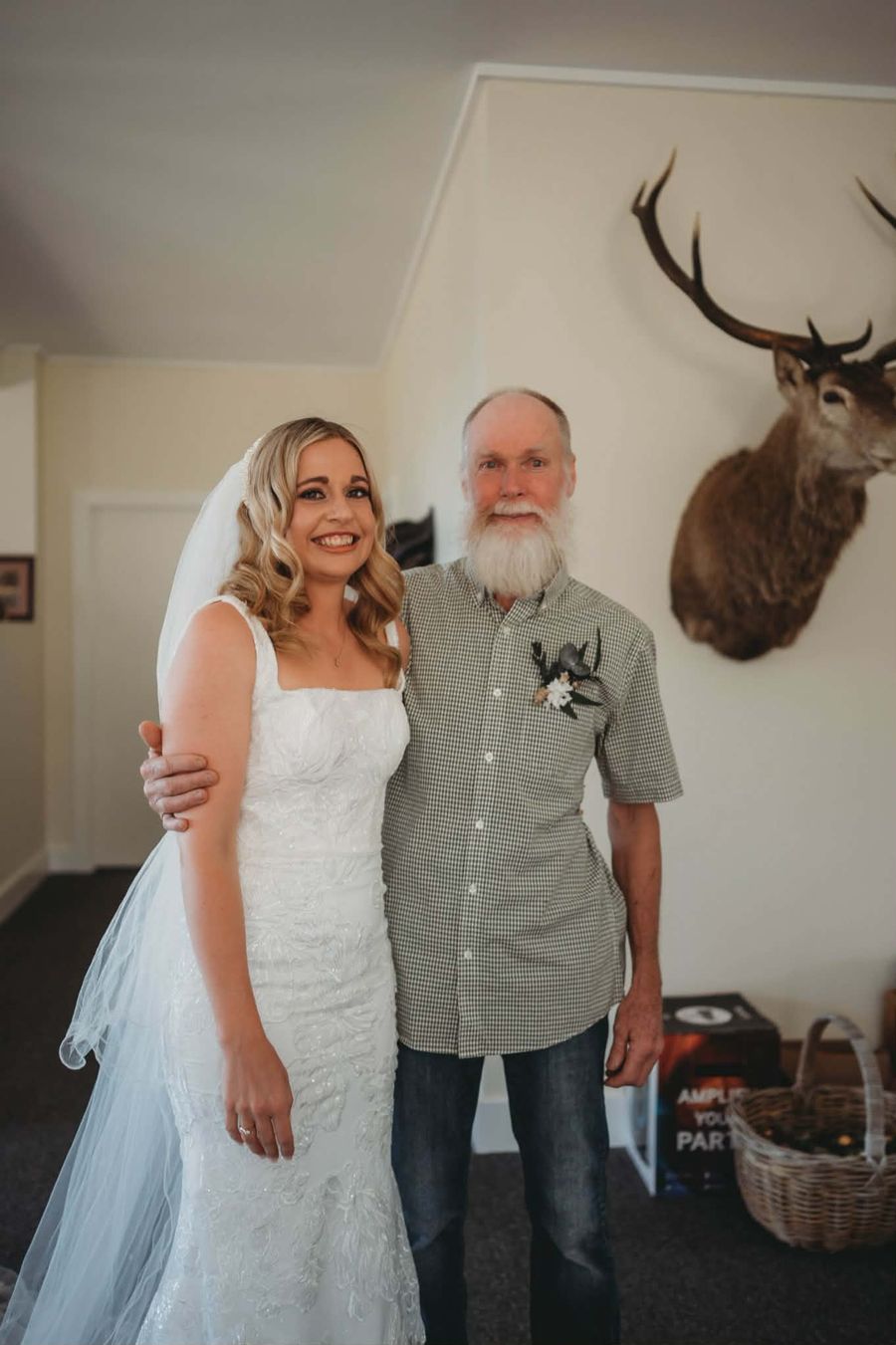 Lilly and her dad on her wedding day, with a red stag mount on the wall behind them