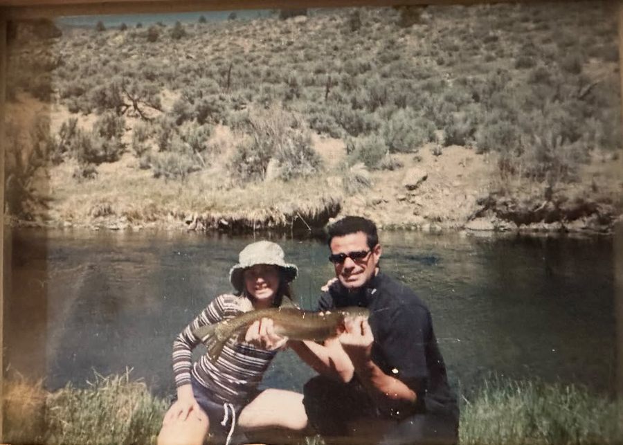 A young Staysha holding a large fish beside a river with a man in sunglasses