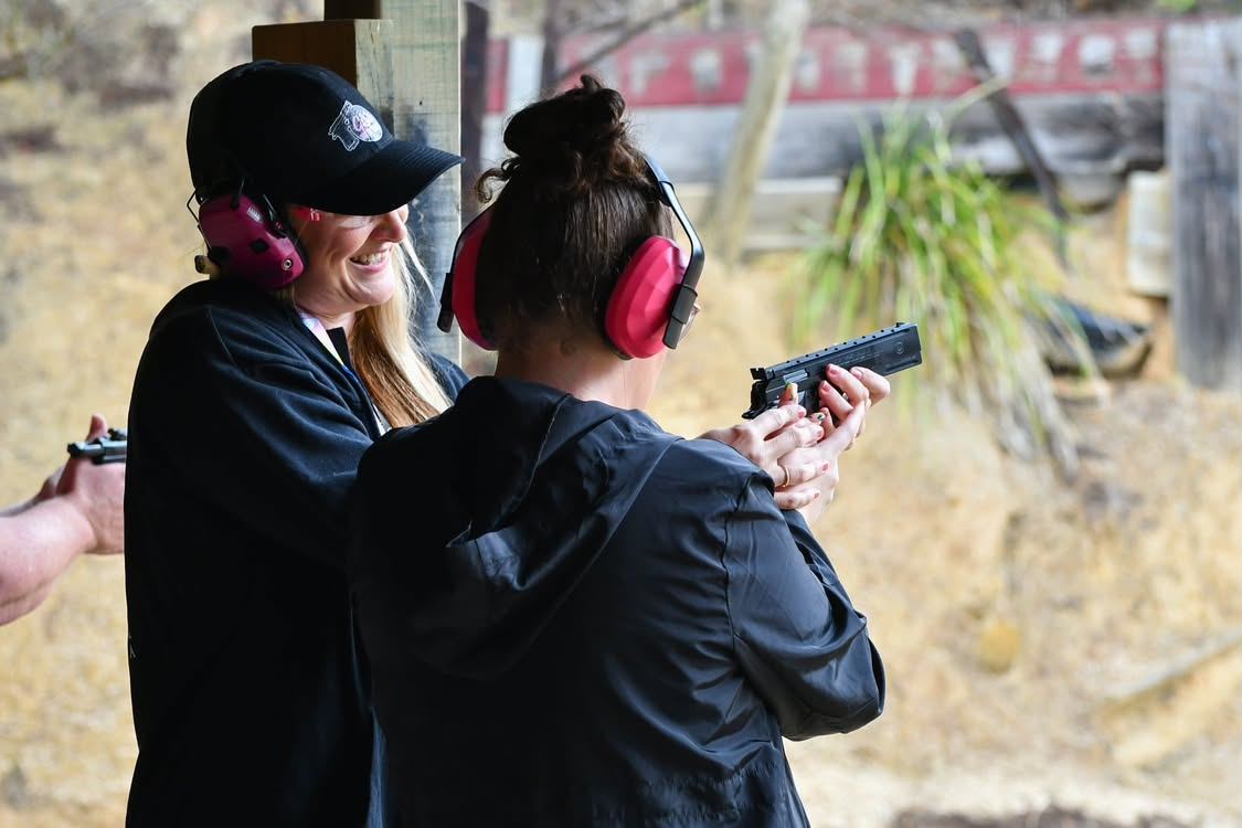 An instructor laughing beside a woman firing a pistol