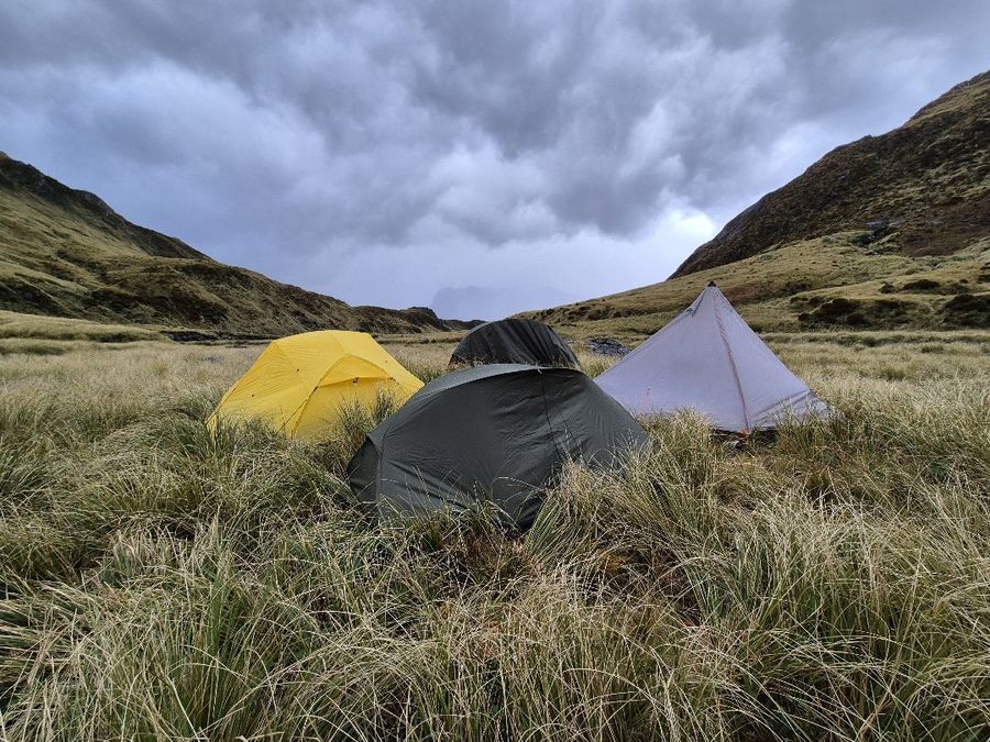 Three tents pitched in NZ tussock under a dramatic stormy sky