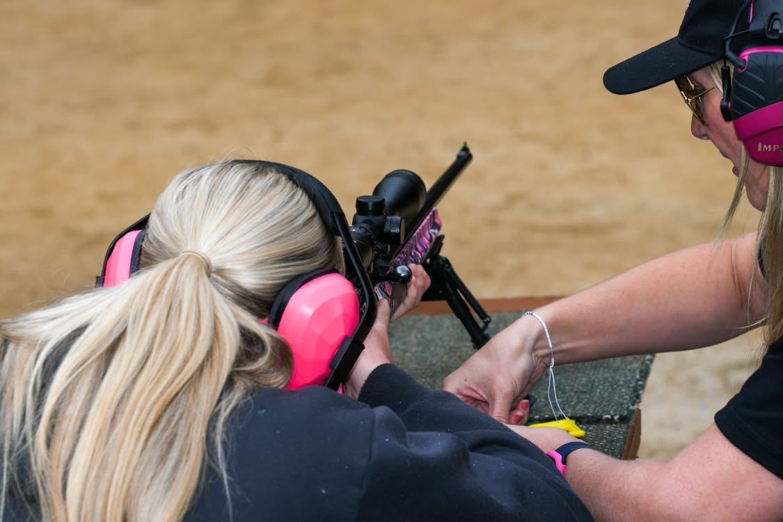 An instructor guiding a shooter on a pink-stocked rifle at the bench