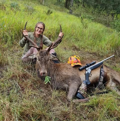 Gaby kneeling behind a red stag with her rifle laid across the antlers